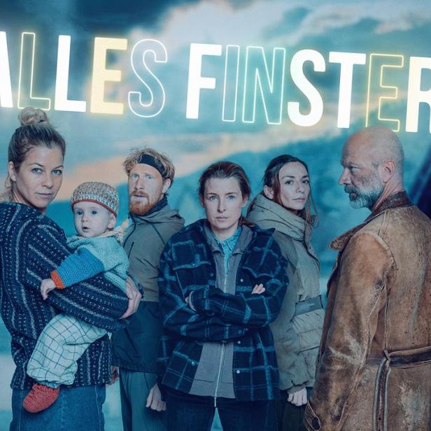 Sechs Personen und ein Baby stehen vor einem dörflichen Hintergrund, darüber steht der weiße Schriftzug „ALLES FINSTER“.